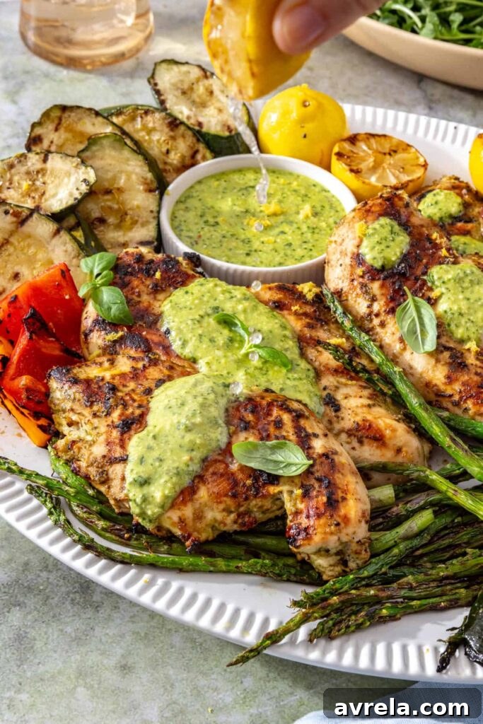 Hand squeezing grilled lemon over pesto chicken and vegetables