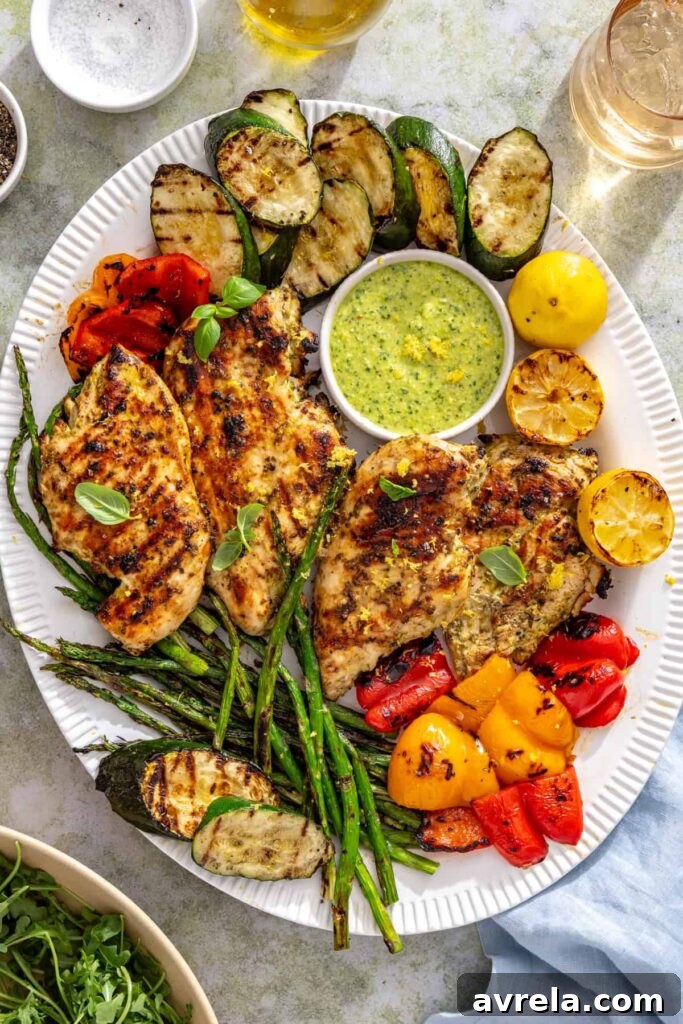 Overhead table setting featuring lemon pesto grilled chicken, grilled vegetables, salad, and summer drinks