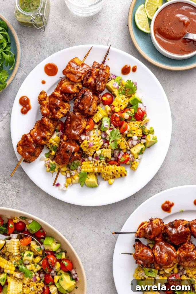 Healthy BBQ chicken skewers served with corn and tomato summer salad