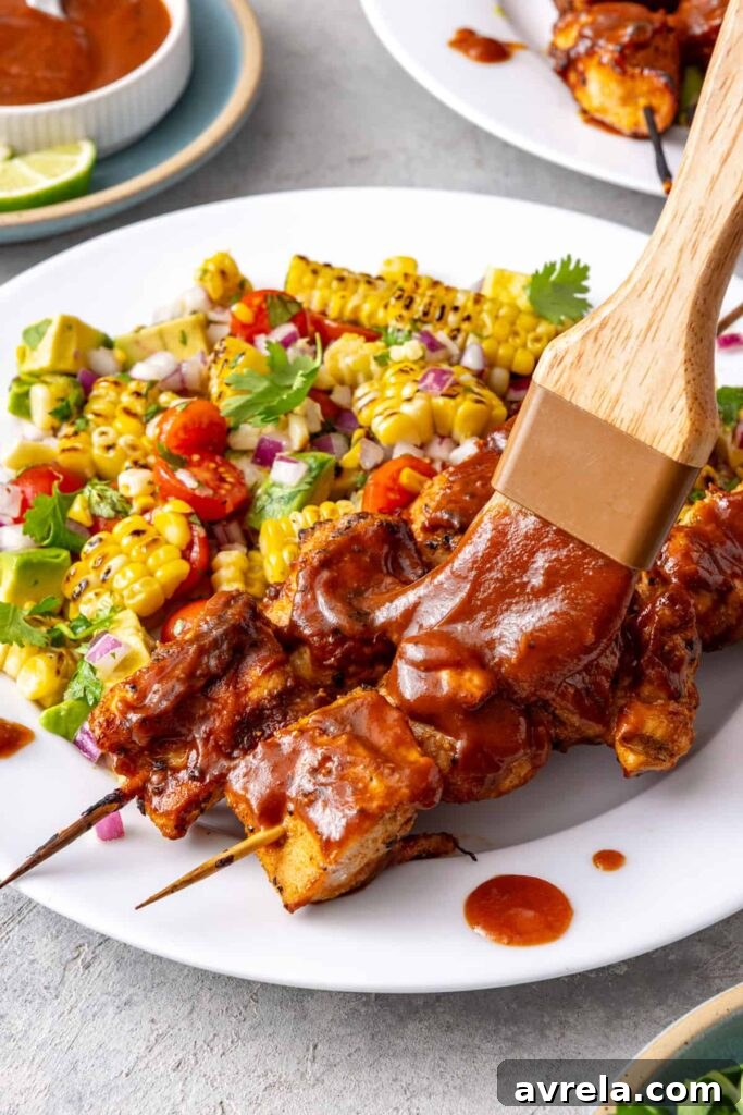 Brushing BBQ sauce onto grilled chicken skewers served with corn and tomato salad