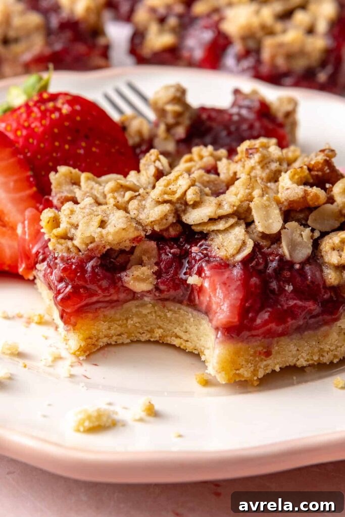 Close-up of a strawberry crumble bar with a fork and fresh strawberries.