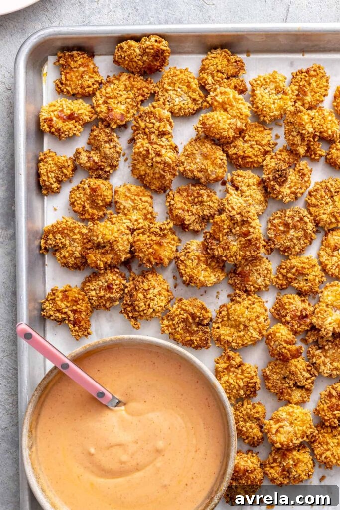 Golden crispy air fryer bang bang shrimp cooling on a baking sheet beside homemade bang bang sauce