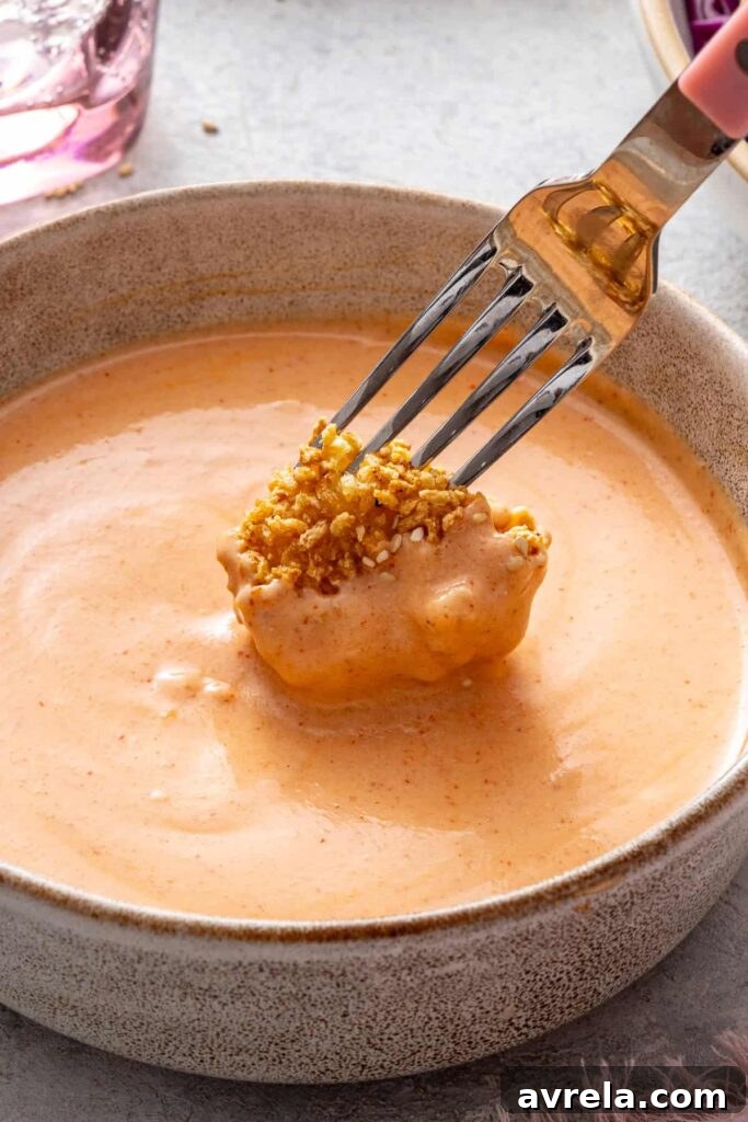 Fork dipping crispy air fryer bang bang shrimp into creamy homemade bang bang sauce.