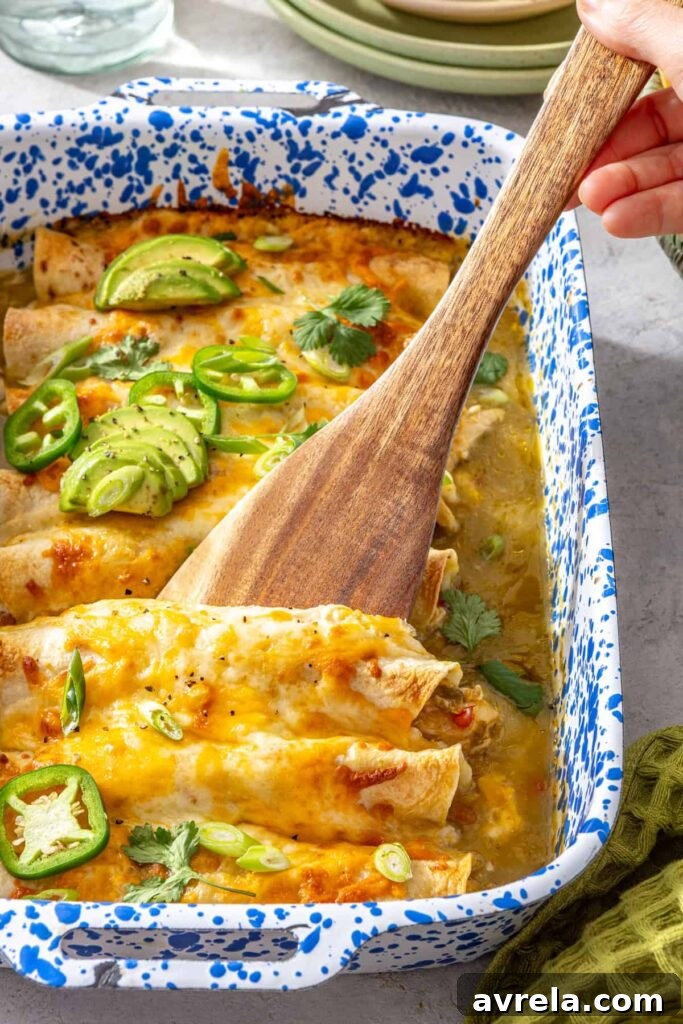 Baked Creamy Chicken Enchiladas with Salsa Verde 7 Wooden spatula lifting a creamy chicken enchilada with melted cheese and salsa verde