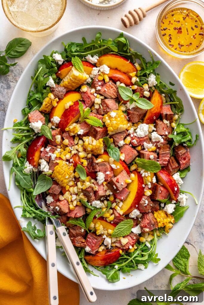 Harissa steak salad with charred peaches, grilled corn, arugula, and feta served in a bowl