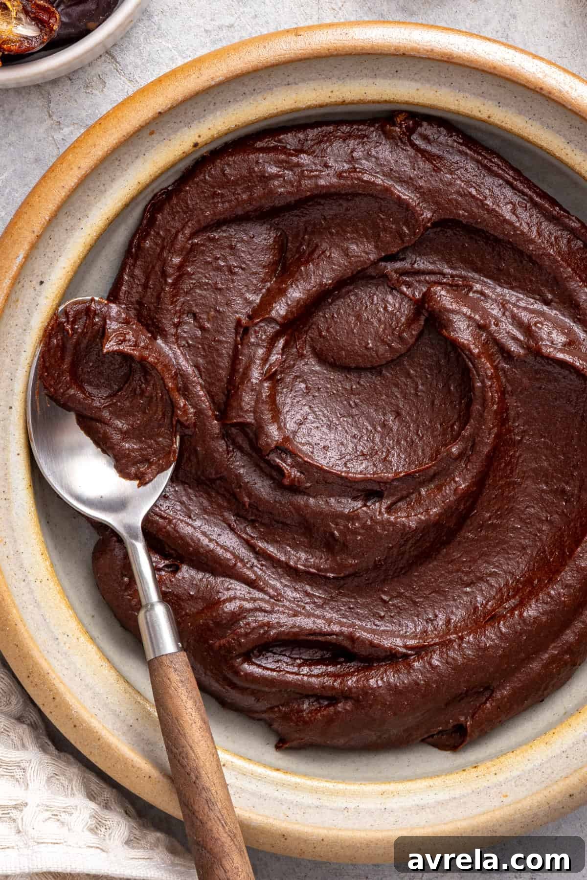 Healthy chocolate frosting made with dates, cacao powder, and coconut cream served in a bowl with a spoon.