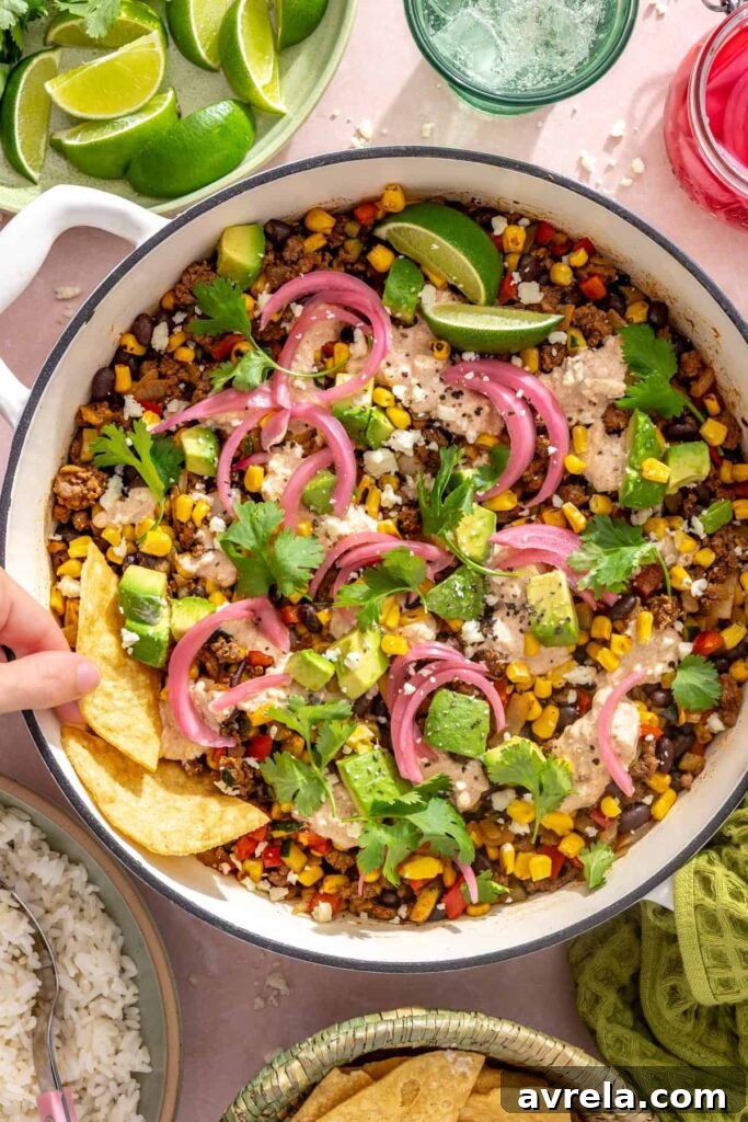 High-Protein Street Corn Taco Skillet One-Pan Dinner 14 Hand dipping tortilla chips into a finished street corn taco skillet
