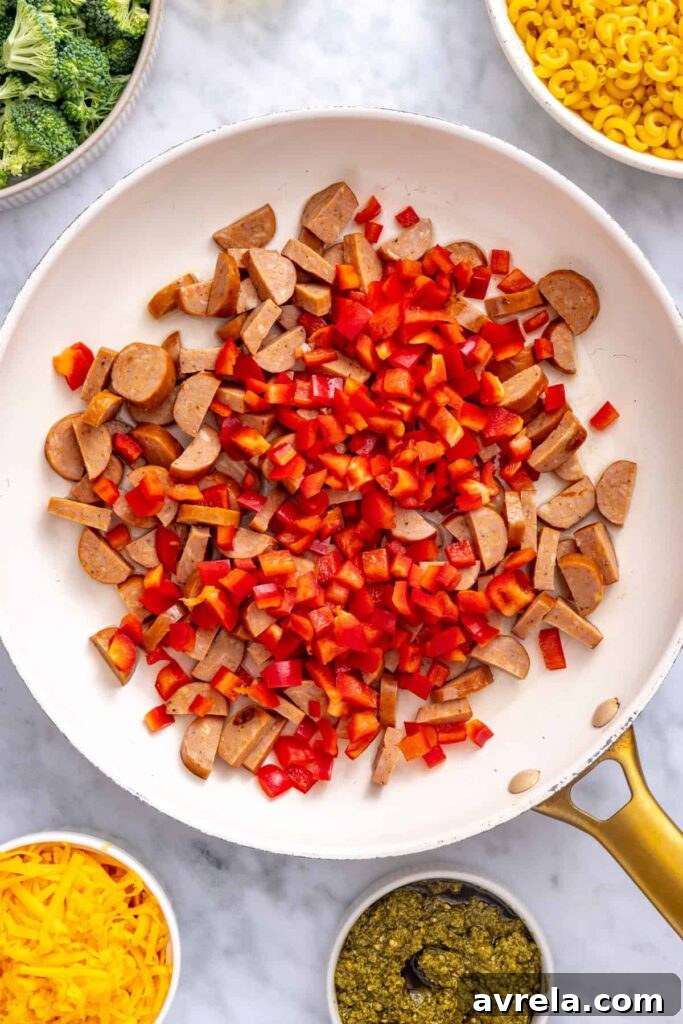 Sliced smoked chicken sausage and diced red bell pepper cooking in a skillet