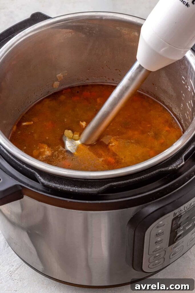 Immersion blender partially blending Instant Pot buffalo chicken chili until creamy