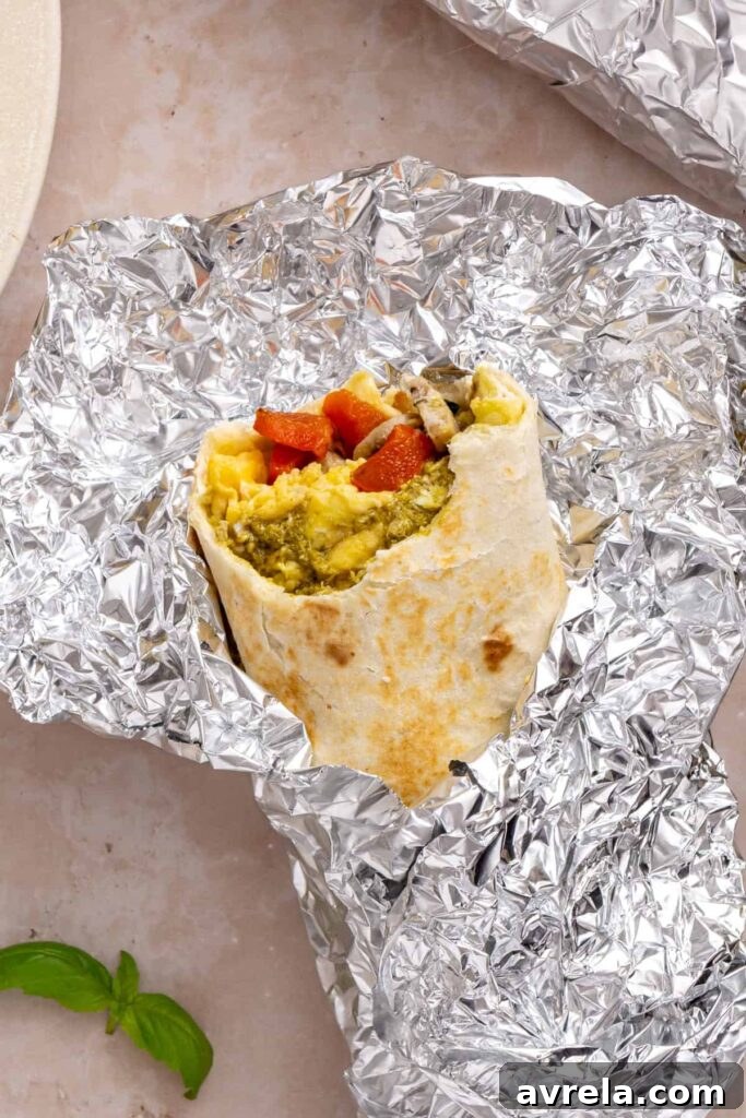 Chicken pesto breakfast burrito cut open to show eggs, chicken sausage, spinach, roasted red peppers and mozzarella