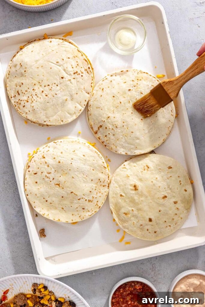 Second tortillas placed over the filling to assemble sheet pan quesadillas and brushing oil over top