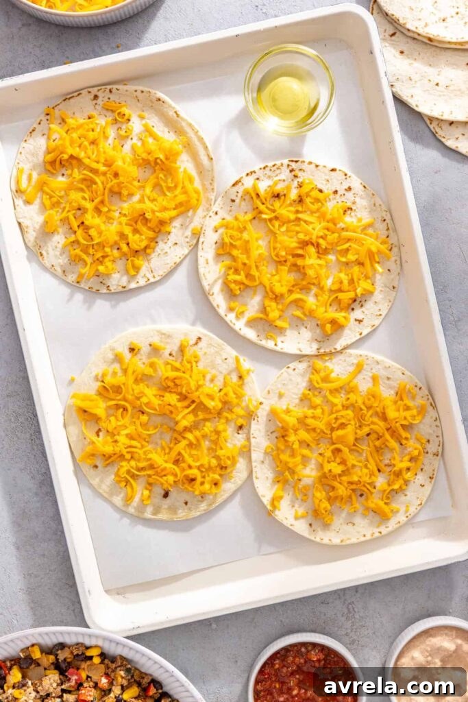 Shredded cheddar cheese sprinkled over tortillas for sheet pan quesadillas